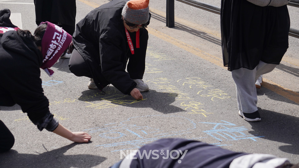 한 시민이 진광수 목사가 발언한 "단결한 민중은 결코 패배하지 않는다"라는 문장을 도로 위에 적고 있다. 뉴스앤조이 엄태빈